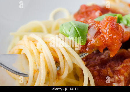 Eine Schüssel Spaghetti Nudeln, Tomatensauce und Basilikum Blätter mit Käse, mit Nahaufnahme von erhöhten Gabel im Vordergrund, eingewickelt in Spaghetti und eingetaucht in sau Stockfoto