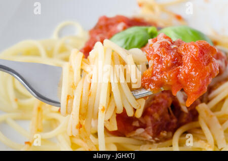 Eine Schüssel Spaghetti Nudeln, Tomatensauce und Basilikum Blätter mit Käse, mit Nahaufnahme von erhöhten Gabel im Vordergrund, eingewickelt in Spaghetti und eingetaucht in s Stockfoto