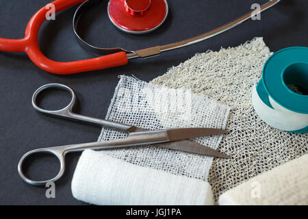 Medizinische Bandagen mit Schere, Heftpflaster und medizinische Stethoskop auf schwarzem Hintergrund. Medizinische Instrumente. Stockfoto