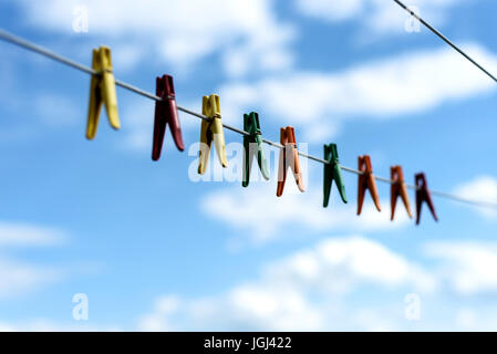 Eine Auswahl an bunten Wäsche Heringe und Wäscheklammern an einer Outdoor-Wäscheleine mit strahlend blauem Himmel und weißen Wolken sommerlich Stockfoto