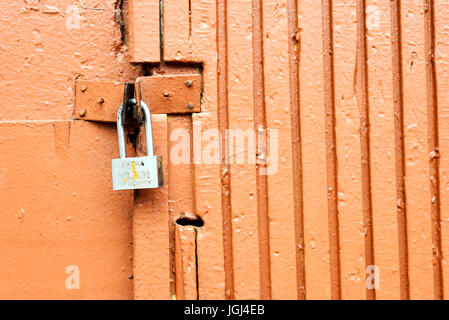 Einzelne Vorhängeschloss verriegeln eine Orange lackiert rustikal Tür aus Holz und Metall hergestellt Stockfoto