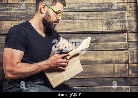 Junger Mann Tischler mit Bart auf einer Bank sitzen Futter ein Brett in einem Workshop Stockfoto