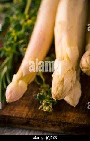 Vertikale Foto mit wenigen Stücken des weißen Spargels. Köstliches Gemüse wird auf dunkle Vintage Schneidbrett aus Holz mit brauner Farbe und grüne Kraut gelegt. Stockfoto