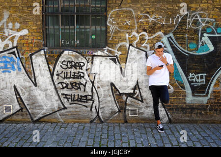 Ein junger Mann rauchen in Spitalfields, im East End von London, während Sms auf seinem Handy Stockfoto