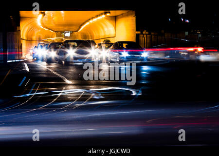 Nachtverkehr auf Straßen der Stadt. Autos in der Warteschlange am Tunnelausgang wartet an Kreuzung beim führen von Fahrzeugen, die bewegte Vergangenheit verlassen Farbe Lichtspuren Stockfoto