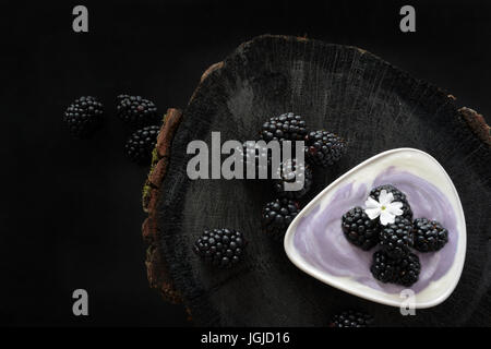Brombeeren mit Joghurt auf schwarzem Hintergrund aus Holz Stockfoto