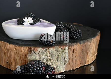 Brombeeren mit Joghurt auf schwarzem Hintergrund aus Holz Stockfoto