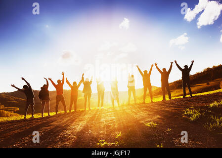 Große Gruppe von Freunden, die Erhöhung der Arme auf Sonnenuntergang zusammen Stockfoto