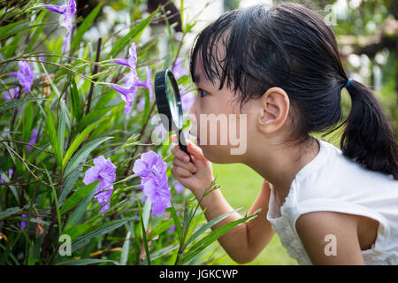Asiatische chinesische Mädchen betrachten Blume durch ein Vergrößerungsglas im Garten