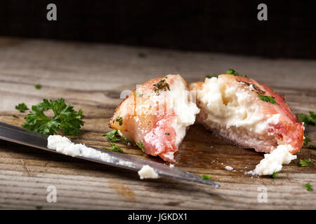 Ziegenkäse, eingewickelt in Speck gebraten auf Holz mit Messer und Petersilie Stockfoto