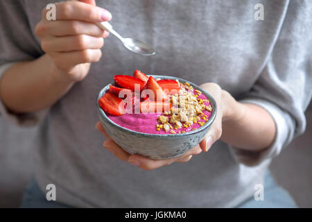 Essen gesundes Frühstück Schale. Acai Smoothie, Müsli, Samen, frische Erdbeeren in blauen Keramikschale in weiblichen Händen. Sauber, Essen, Diät, Entgiftung, v Stockfoto