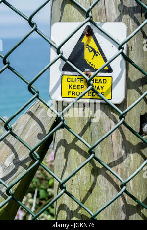 Dreieckige Gefahr Warnzeichen hinter einem Maschendrahtzaun, Information der Öffentlichkeit von Klippen rund um Newquay in Cornwall.Metaphor für Post-Austritt UK? Stockfoto