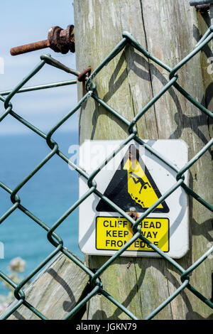 Dreieckige Gefahr Warnzeichen hinter einem Maschendrahtzaun, Information der Öffentlichkeit von Klippen rund um Newquay in Cornwall.Metaphor für Post-Austritt UK? Stockfoto