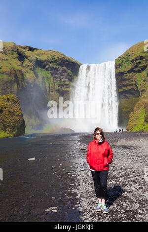 Weibliche Touristen in einer roten Jacke posiert am Skogafoss Wasserfall in Island Stockfoto