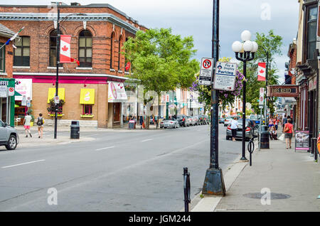 Kingston, Kanada - 23. Juli 2014: Downtown City im Sommer mit kanadischen Flaggen und Menschen zu Fuß auf der Hauptstraße Stockfoto