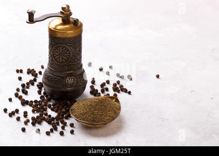 Schwarze Pfefferkörner, Pulver und alte Vintage Mühle auf weißen Stein Hintergrund, Ansicht von oben Stockfoto