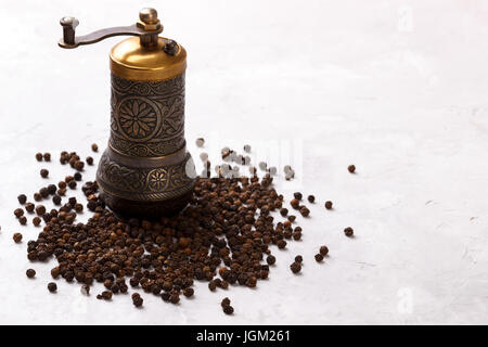 Schwarze Pfefferkörner und alte Vintage Mühle auf weißen Stein Hintergrund, Ansicht von oben Stockfoto