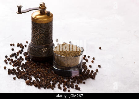 Schwarze Pfefferkörner, Pulver und alte Vintage Mühle auf weißen Stein Hintergrund, Ansicht von oben Stockfoto