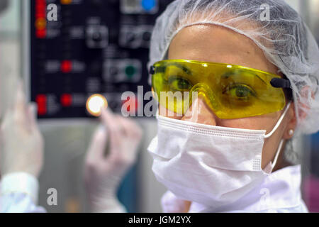 Arbeitnehmerin tragen gelbe Schutzbrille, Blick in die Kamera. Pharmazeutischer Arbeiter über die Systemsteuerung pharmazeutische Maschine. Stockfoto