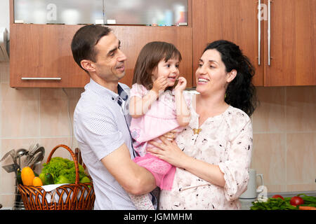 Familienbild in Küche Interieur mit frischem Obst und Gemüse, gesunde Ernährung Konzept, schwangere Frau, Mann und Kind Mädchen Stockfoto