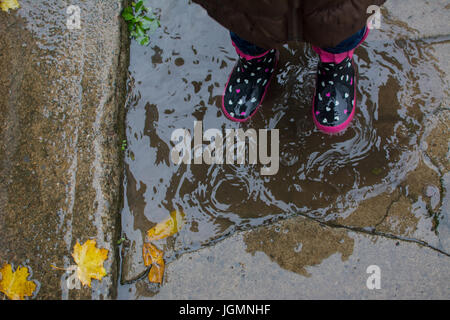 Ein kleines Kind steht im regen Stiefel in einer Pfütze im Herbst. Stockfoto