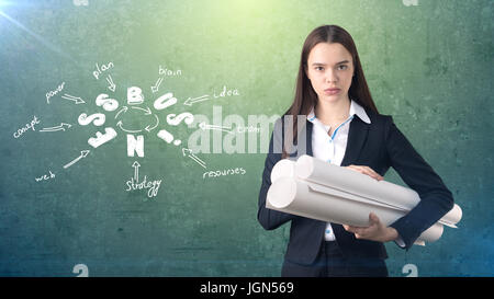 Frau in einem Anzug in der Nähe von Wand mit Blaupausen und ein Geschäft Ideenskizze drauf gezogen. Konzept eines erfolgreichen Unternehmens. Stockfoto