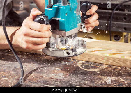 Close-up, wie eine moderne grüne Fräsmaschine arbeiten auf Holz, auf einem Holztisch Hintergrund Stockfoto