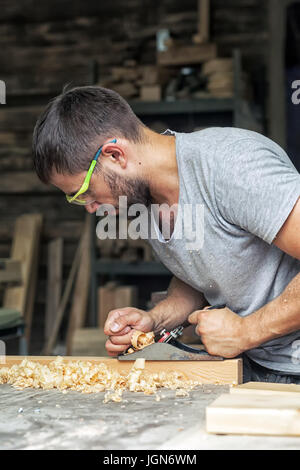 Ein junger Mann mit Bart und Sonnenbrille durch Beruf, der Zimmermann hält einen Black Jack Flugzeug in die Hände und ist gleich ein Brett, in den hinterg Stockfoto
