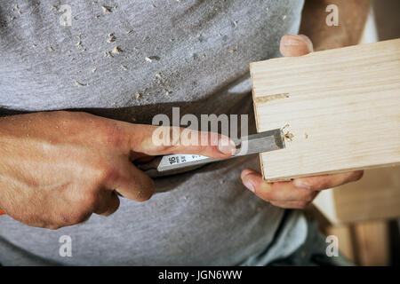 Eine Nahaufnahme, wie ein junger Mann in einem grauen T-Shirt ist mit einer Schlaufe in der Hand und die Verarbeitung einer Holz- Produkt Stockfoto