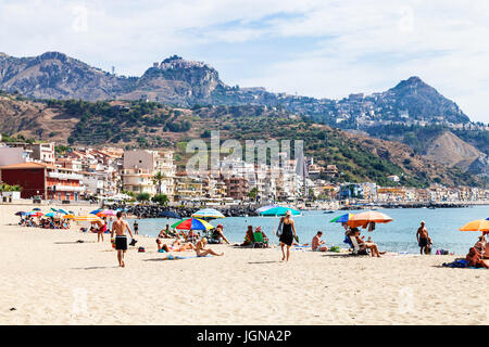 GIARDINI NAXOS, Italien - 28. Juni 2017: Urlauber am Sandstrand in Giardini-Naxos-Stadt und Blick auf Taormina Stadt am Kap. Giardini Naxos ist am Meer r Stockfoto