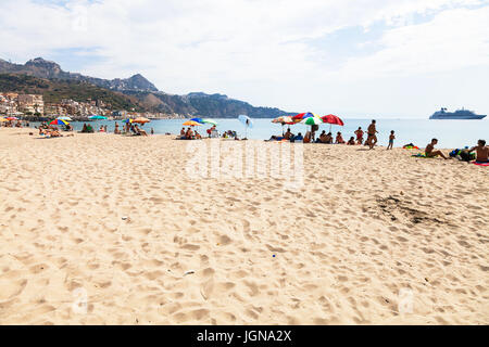 GIARDINI NAXOS, Italien - 28. Juni 2017: Menschen am städtischen Sandstrand in Giardini-Naxos-Stadt und Blick auf Taormina Stadt am Kap. Giardini Naxos liegt am Meer Stockfoto