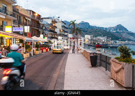 GIARDINI NAXOS, Italien - 28. Juni 2017: Menschen, Geschäfte und Pkw-Verkehr auf der Uferpromenade in Giardini-Naxos-Stadt in Sommerabend. Giardini Naxos liegt am Meer Stockfoto