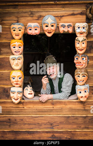 Holzmaske Carver in einem Fenster umrahmt von bemalten hölzernen Masken Holzmaske Carving Workshop, Bad Aussee, Steiermark, Österreich Stockfoto