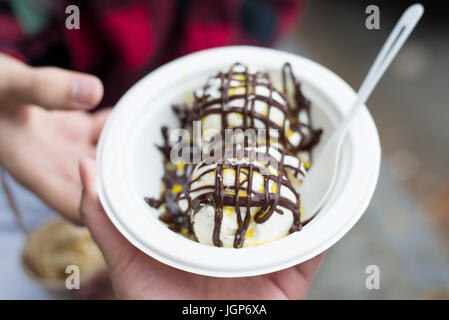 Hand mit einem Eisbecher in Olivenöl und Schokolade Sirup abgedeckt Stockfoto