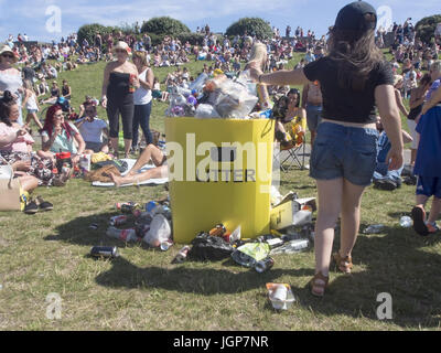 Ein junges Mädchen wirft Müll in einem überquellenden Abfallbehälter in einem öffentlichen Park mit Müll auf dem Boden daneben liegen. Stockfoto