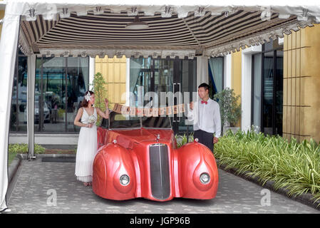 Frisch verheiratetes junges Paar posieren für Hochzeitsfotos neben einem Cadillac Auto. Thailand-Südostasien Stockfoto
