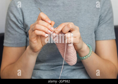 Eine junge Frau strickt eine Häkeln mit einem gestrickten Pullover aus Wolle. Stockfoto