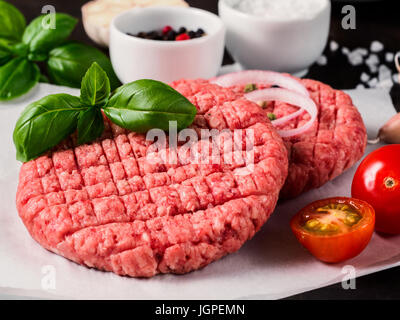 Nahaufnahme der beiden rohes Fleisch Steak Schnitzel für Burger mit Gemüse, Gewürzen und frischem Basilikum. Hausgemachte Burger zu machen. Stockfoto