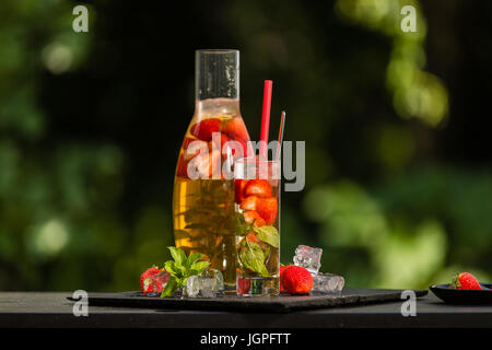 Hausgemachte Erdbeer Eistee im Garten. Eis, Erdbeeren, Minze und Zitronenmelisse Blätter und grüner Tee. Stockfoto