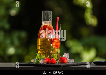 Hausgemachte Erdbeer Eistee im Garten. Eis, Erdbeeren, Minze und Zitronenmelisse Blätter und grüner Tee. Stockfoto