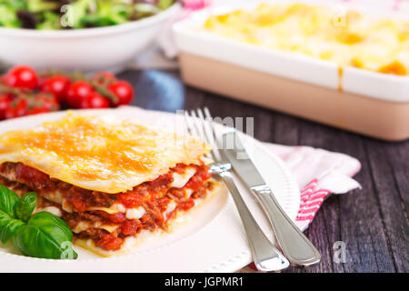 Eine Portion hausgemachte Lasagne auf einer Platte auf einem hell erleuchteten Tisch. Stockfoto