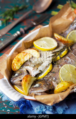 Ein Ofen gebratene Forellen in einem hohen Topf auf einem rustikalen Tisch. Mit Karotten und Kartoffeln auf der Seite. Stockfoto