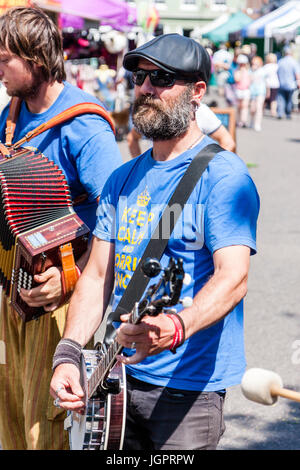 Folk Musiker Tänzer. Kaukasische Mann mit Bart, 40s, trägt eine Kappe und T-Shirt und spielen das Banjo. Mitglied des Königlichen Freiheit Morris Seite. In Street, strahlendem Sonnenschein. Stockfoto