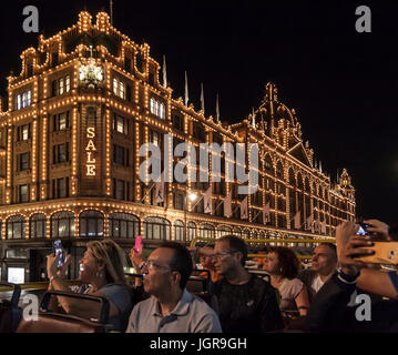 Eine Gruppe von Touristen die beleuchtete Kaufhaus Harrods in Knightsbridge, London, während eines Nacht Cabrio Bus fahren in der Stadt. Stockfoto