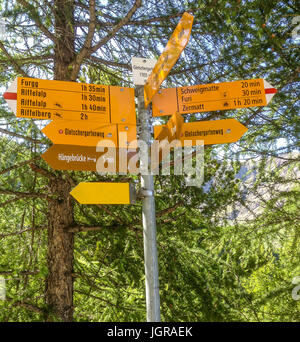 Gelbe Wegweiser mit Wegbeschreibungen zu verschiedenen Wanderwegen in Matterhorn, Zermatt, Schweiz, Europa. Stockfoto