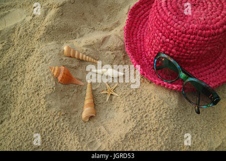 Lebendige rosa farbigen Strohhut und Sonnenbrille am tropischen Sandstrand mit vielen kleinen Muscheln, Thailand Stockfoto
