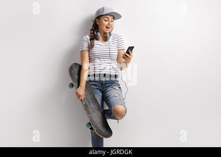 Teenager-Mädchen mit einem Telefon und Skateboard an eine Wand gelehnt Stockfoto