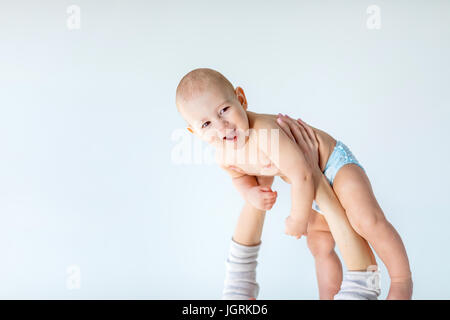 Seitenansicht des entzückenden jungen über den Kopf halten Mutter isoliert auf grau, 1 Jahr alt Baby Konzept Stockfoto