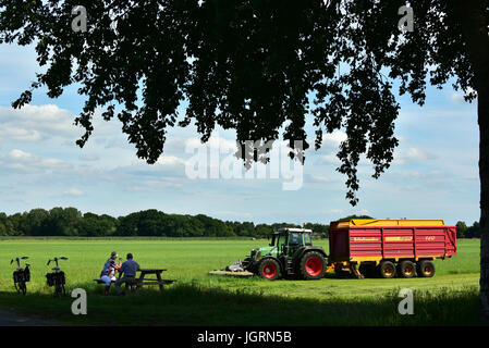 Touristen auf der Suche an einen Traktor Rasenmähen und direkt in einen Ladewagen Futter sammeln. Stockfoto