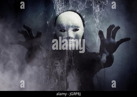 Mysteriöse Frau in schwarz tragen weiße Maske versteckt hinter Spinnennetz, beängstigend Hintergrund für Bucheinband Stockfoto